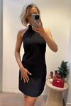 Model showcasing a sleek black halter-neck dress with a fitted silhouette, perfect for elegant evening events or formal occasions, styled with subtle accessories and a festive background